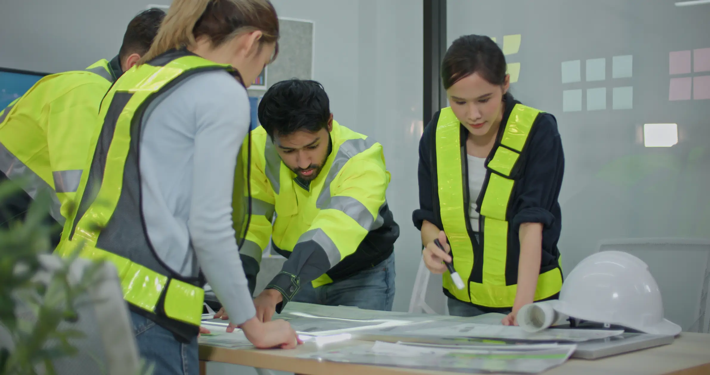 A group of engineers in high vis jackets surveying plans in an indoor location